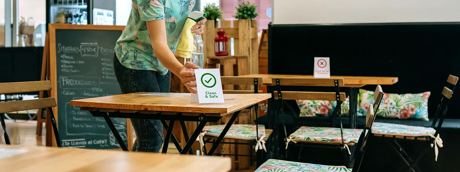 Kaféanställd ställer fram en Clean & Safe-skylt efter rengöring