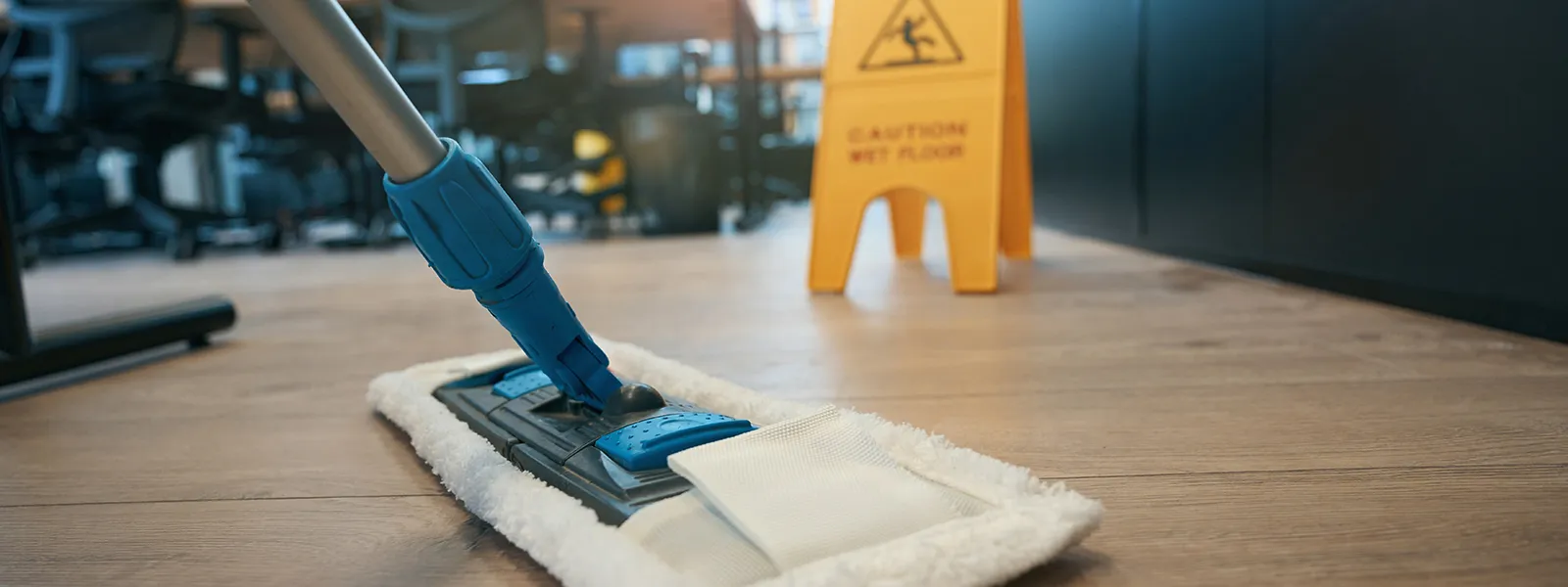 Moppning av trägolv på kontor med varningsskylt i bakgrunden