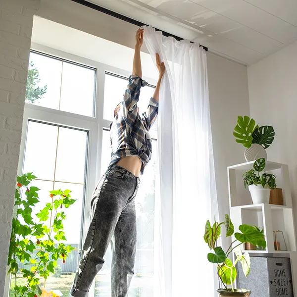 Kvinna hänger upp en gardin framför ett fönster
